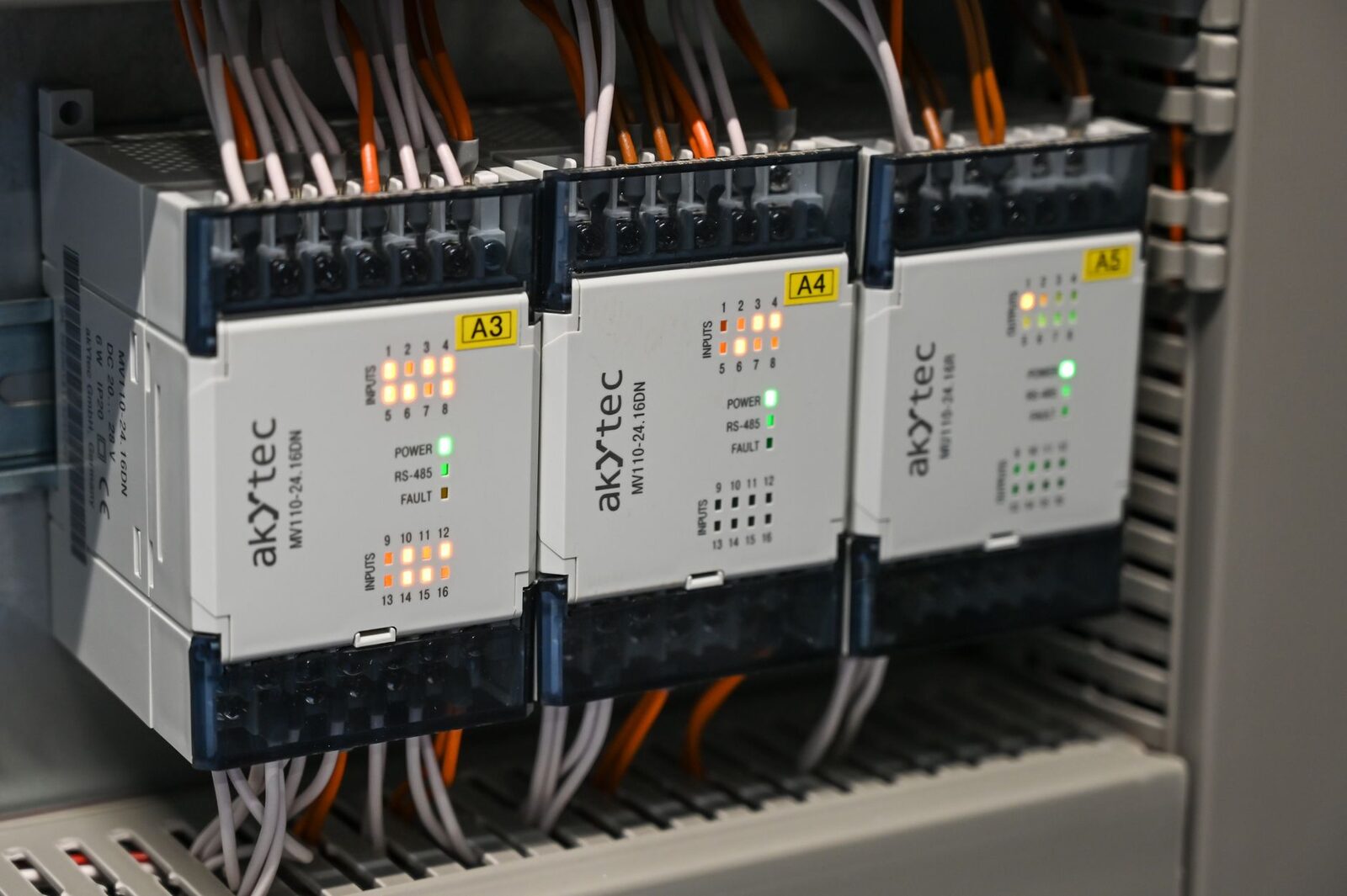 Three industrial input and output modules mounted in a control cabinet with lit input indicators and wired terminals